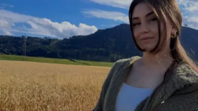 Frau steht auf einem Feld mit Bergen und blauem Himmel im Hintergrund.