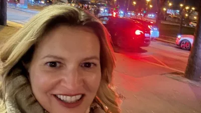 Lächelnde Frau macht ein Selfie bei Nacht in Paris, im Hintergrund ist der beleuchtete Eiffelturm zu sehen.