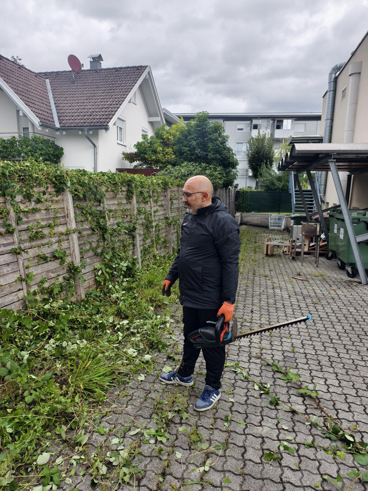 Mann bei Gartenarbeiten im Außenbereich mit Heckenschere, umgeben von geschnittenen Ästen und Grünpflanzen