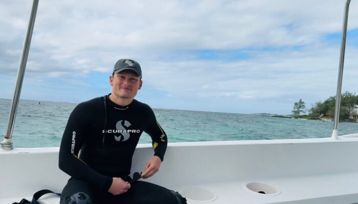 Ein Mann im Neoprenanzug sitzt auf einem Boot am Meer.
