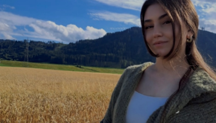 Eine junge Frau steht in einem Kornfeld. Im Hintergrund sind Berge zu sehen.