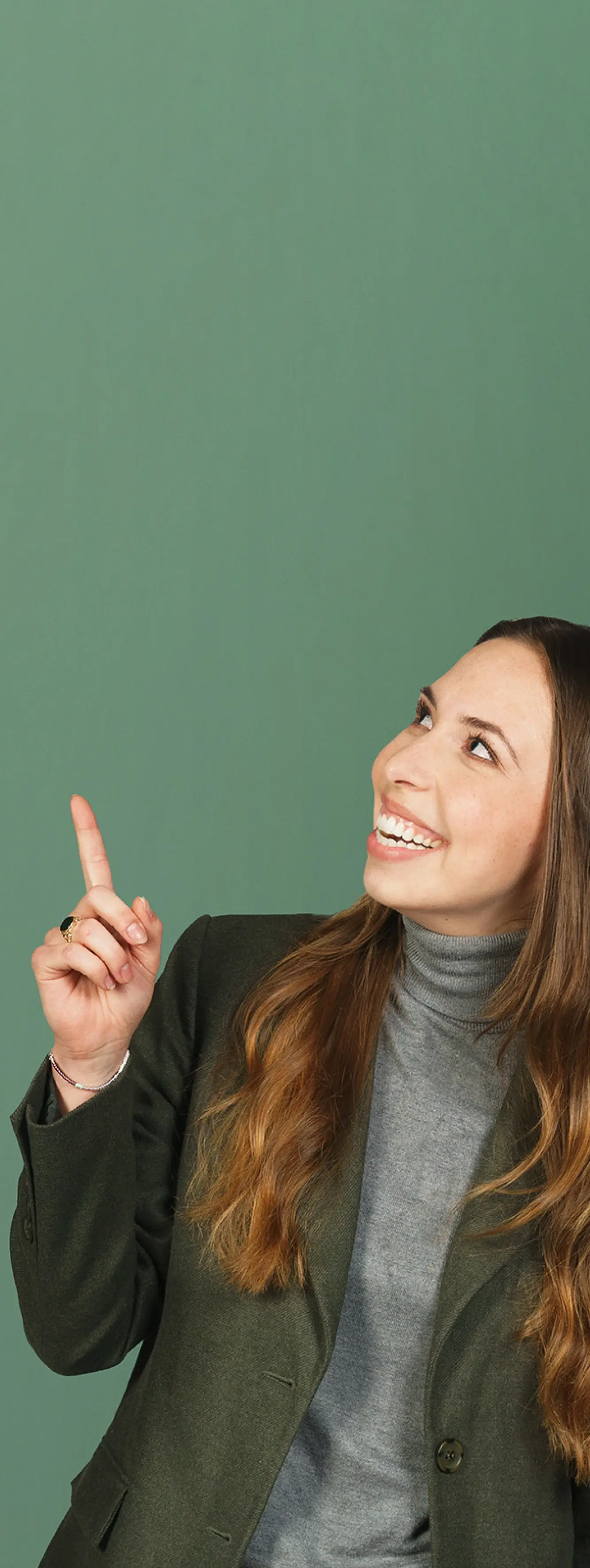 Lächelnde Frau im Business-Outfit, die vor einem grünen Hintergrund nach oben zeigt.