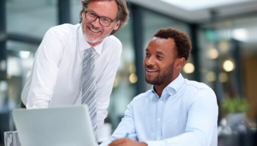 Eine erfahrene Führungskraft und ein jüngerer Geschäftsmann im Gespräch während eines professionellen Meetings in einem modernen Unternehmensbüro.