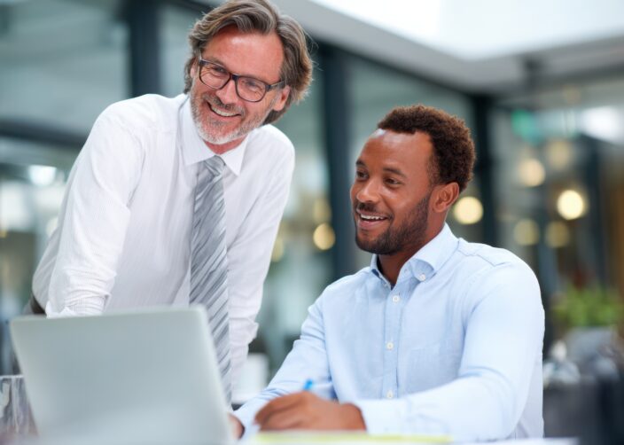 Eine erfahrene Führungskraft und ein jüngerer Geschäftsmann im Gespräch während eines professionellen Meetings in einem modernen Unternehmensbüro.