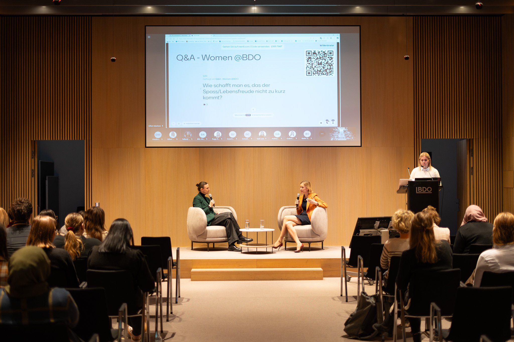 Zwei Frauen im Gespräch auf einer Bühne bei der Veranstaltung „Q&A – Women @BDO", im Hintergrund eine Leinwand mit eingeblendeten Publikumsfragen.